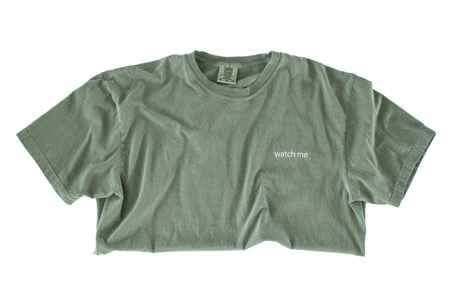 Green t-shirt with 'watch me' text on a white background
