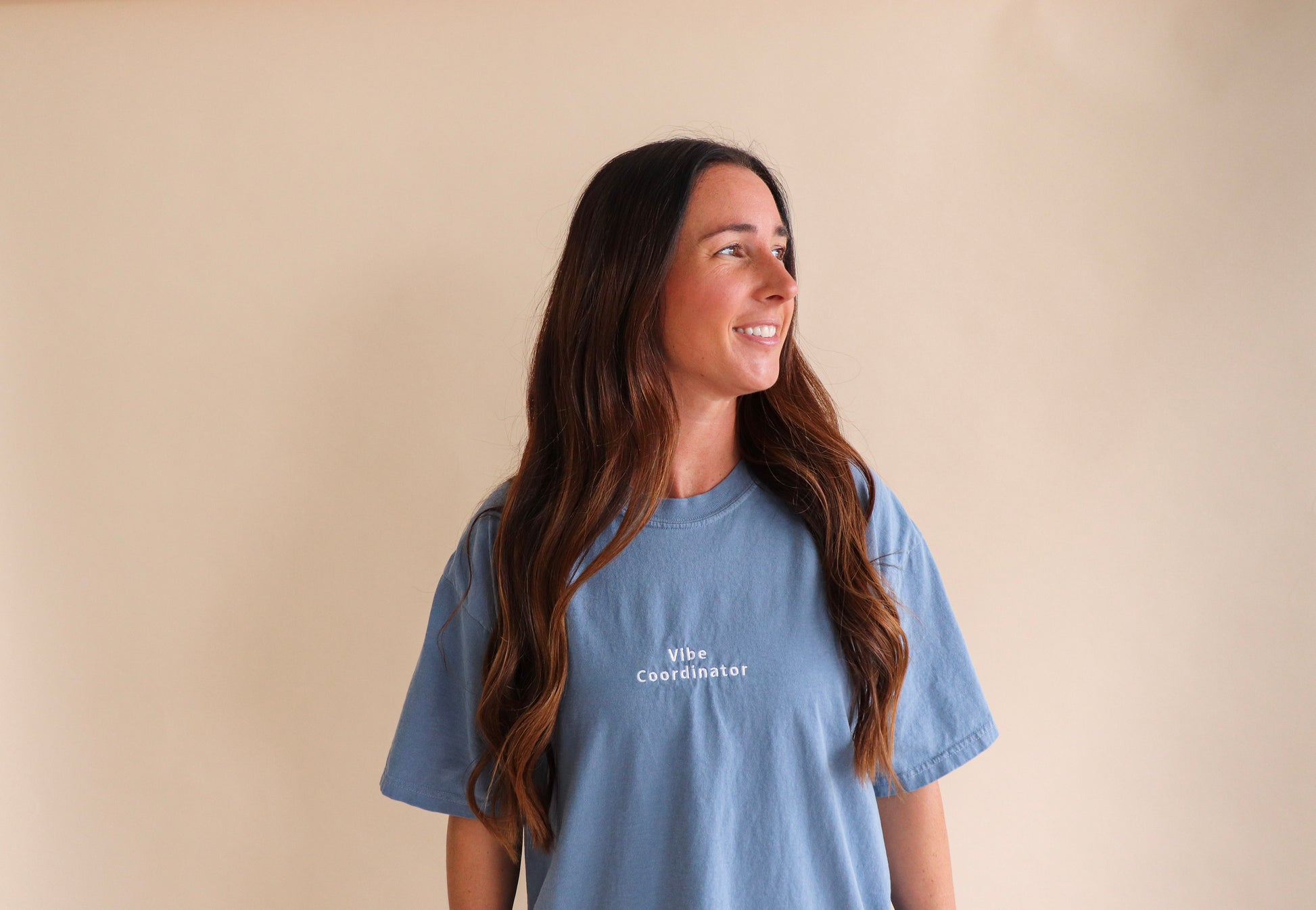 Woman wearing a blue t-shirt with 'Vibe Coordinator' text against a beige background