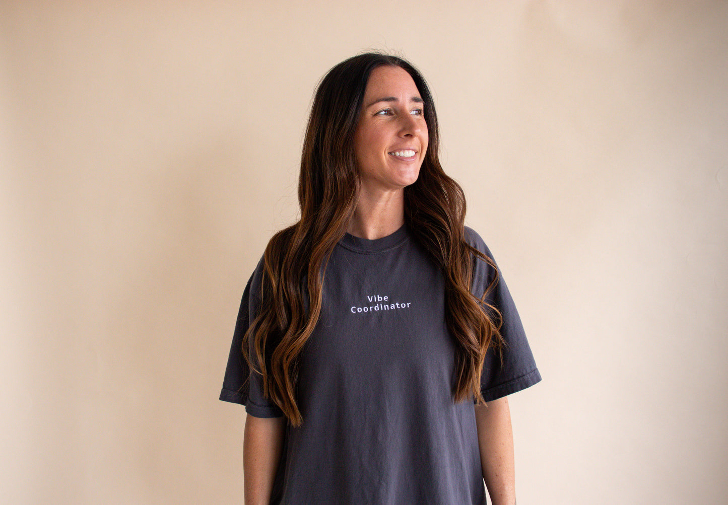 Woman wearing a dark gray t-shirt with text saying vibe coordinator on a beige background