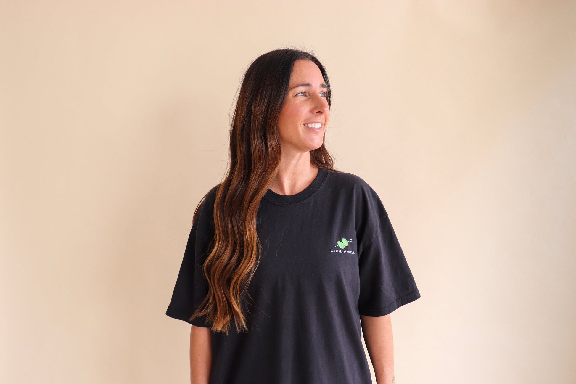 Woman wearing a black t-shirt Extra, Always embroidery on a beige background