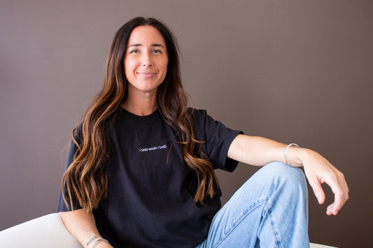 Woman wearing a black t-shirt with text saying I said what i said, sitting against a plain background